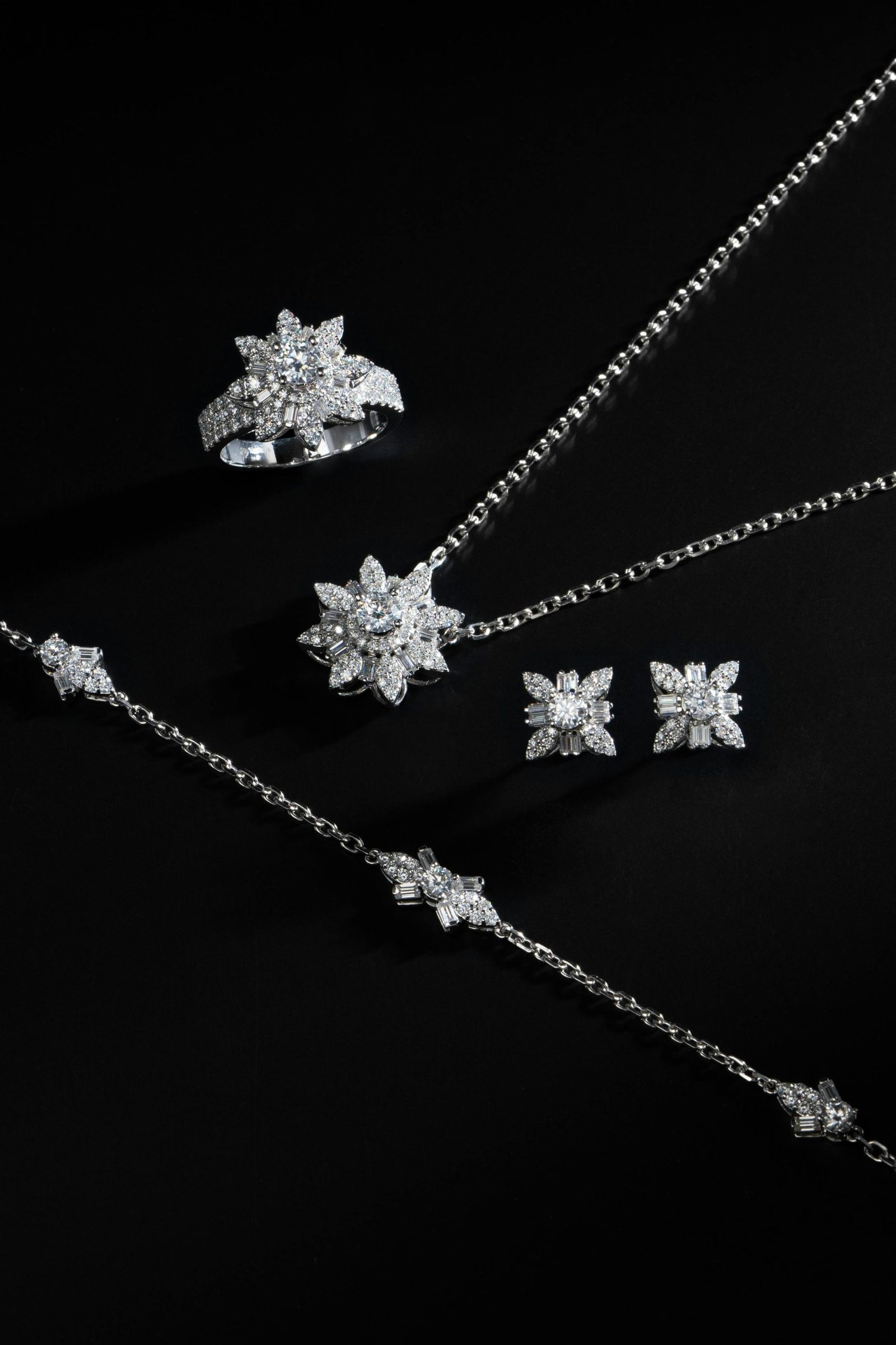 Luxurious silver jewelry set featuring necklace, earrings, and a ring on a black background.